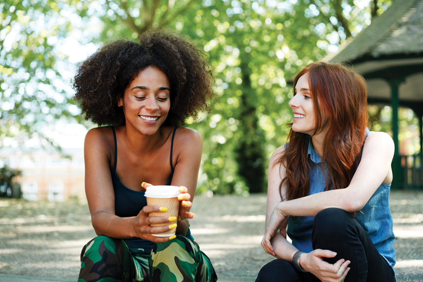Two women sitting. One has a cup of coffee.