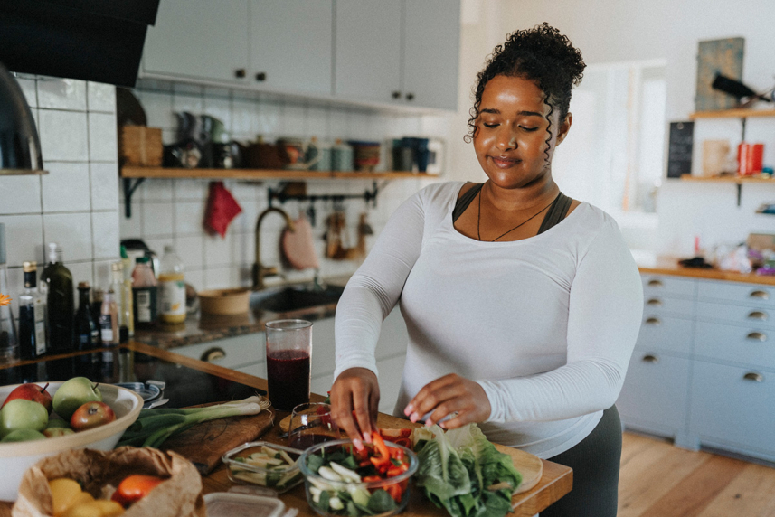 A woman standing in a kitchen with a counter full of fruits and vegetables